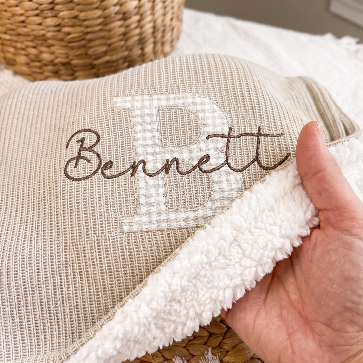Close-up of beige knit sherpa baby blanket showing the plush sherpa back and embroidered name Bennett