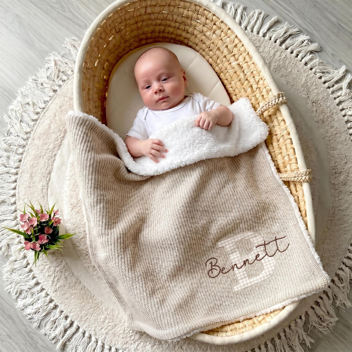 Baby lying in a woven basket under a beige personalized sherpa blanket with applique letter B and name Bennett