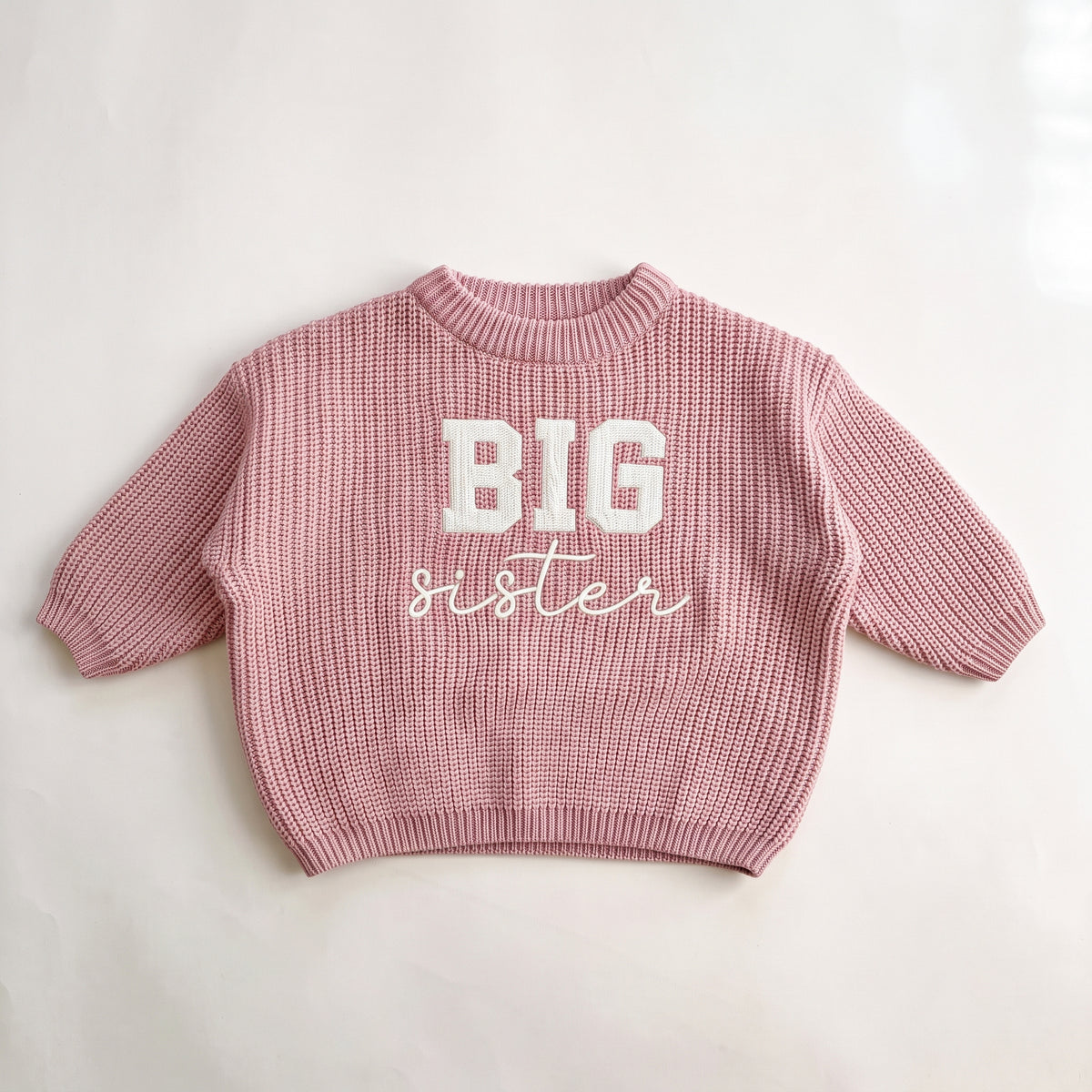 Pink chunky knit baby sweater with BIG sister embroidery, laid flat