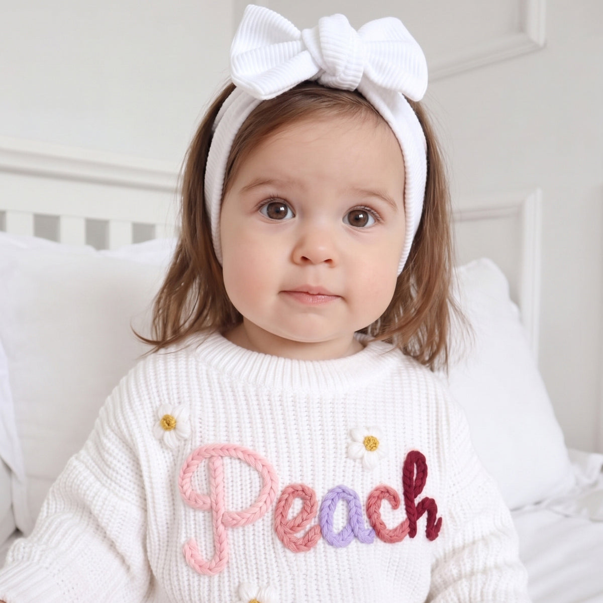 Toddler girl wearing a white sweater with hand embroidered name Peach in pink and purple yarn