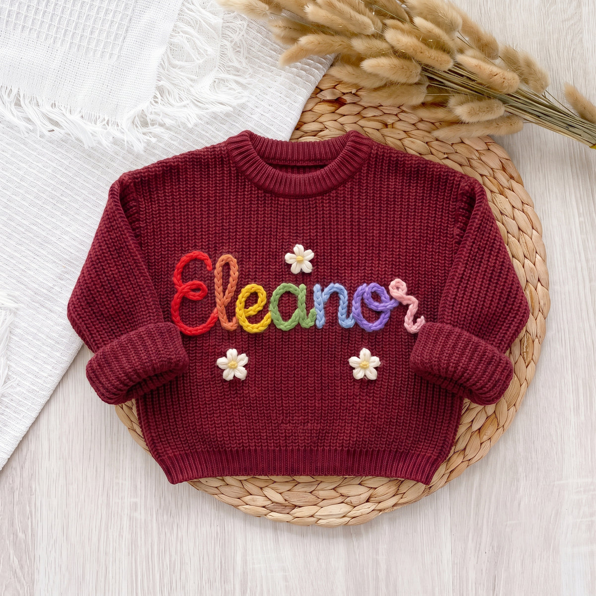 Red personalized sweater with hand embroidered multicolor yarn name Eleanor and flowers, laid flat