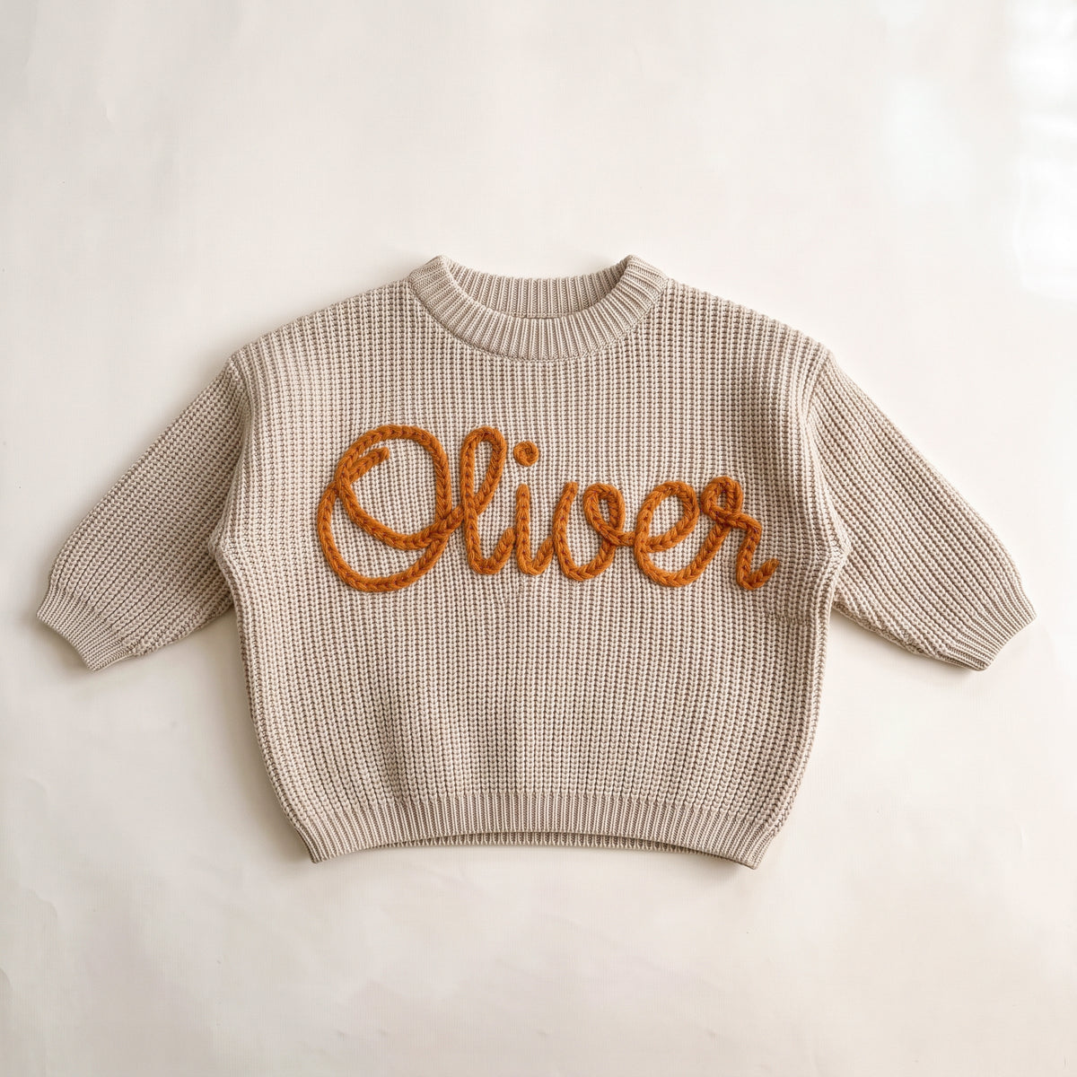 Beige personalized baby sweater with hand embroidered name Oliver in orange chunky yarn, laid flat