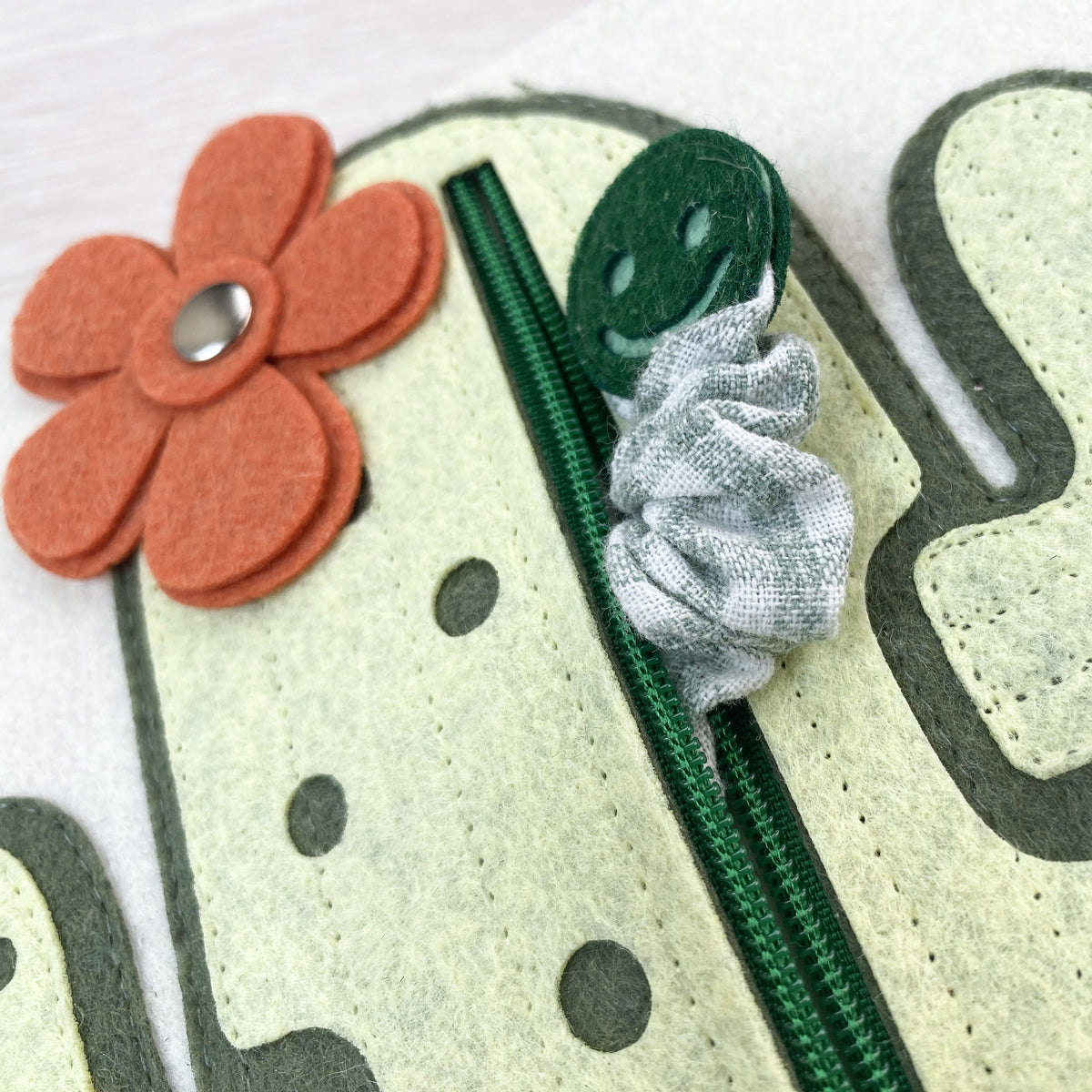 Close-up of soft felt cactus page with green zipper, hidden worm and orange felt flower in a quiet book