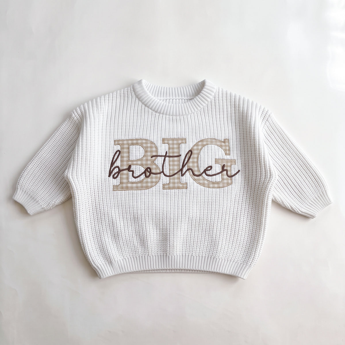 White knit sweater with beige gingham BIG applique letters and brother embroidered in navy script, laid flat