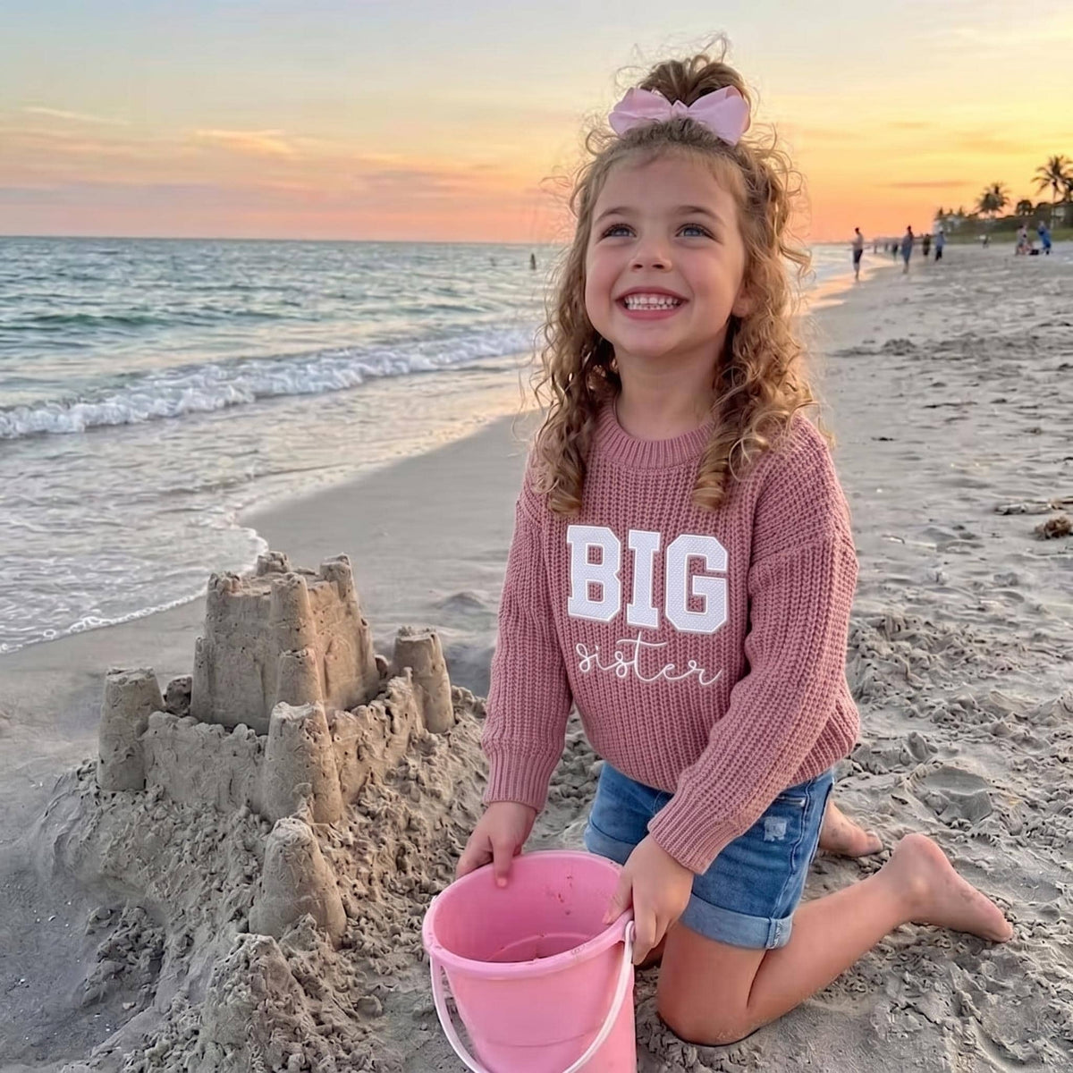 Girl on the beach wearing pink BIG sister embroidered sweater