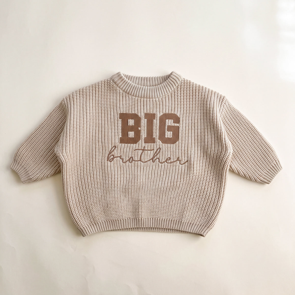 Beige chunky knit baby sweater with BIG brother embroidery, laid flat