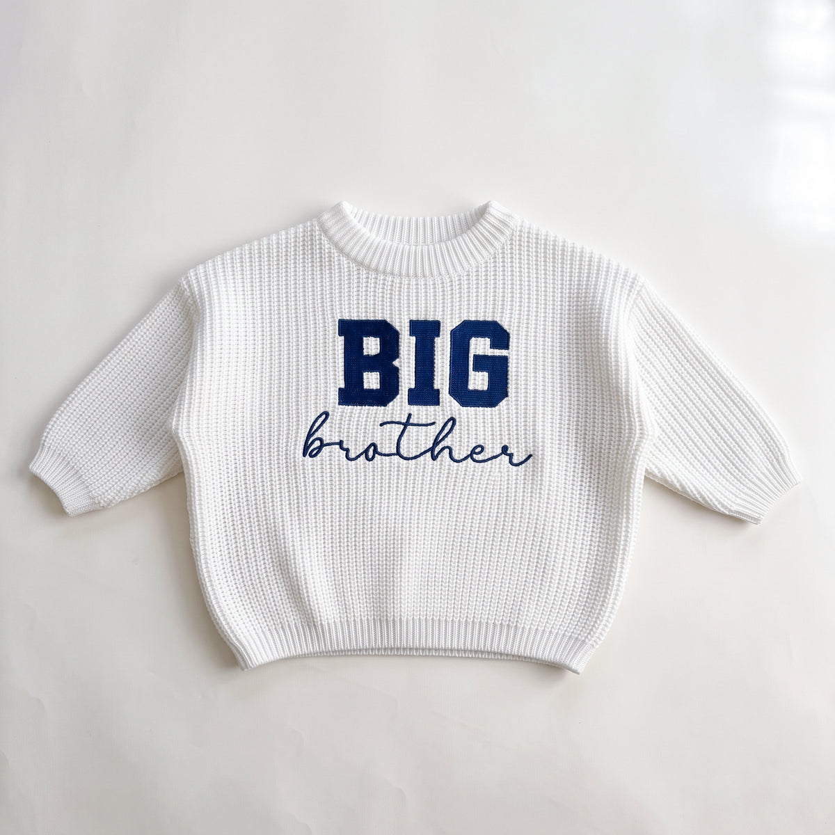 White chunky knit baby sweater with BIG brother embroidery, laid flat