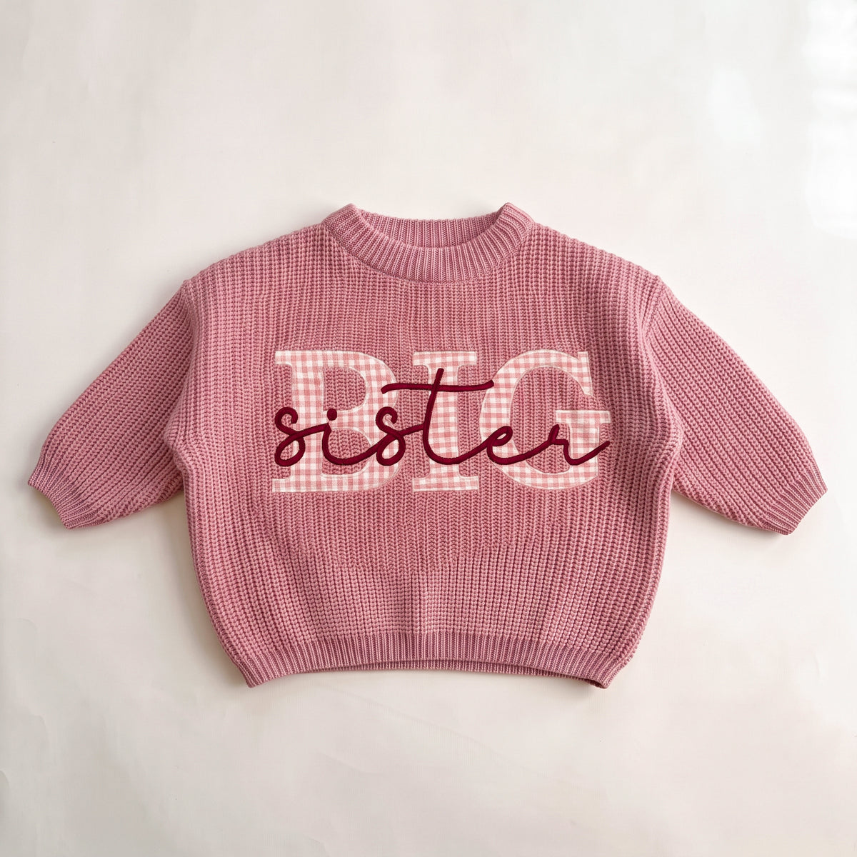 Pink knit sweater with pink gingham BIG applique letters and sister embroidered in burgundy script, laid flat