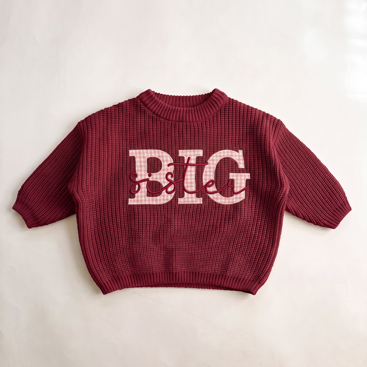 Red knit sweater with pink gingham BIG applique letters and sister embroidered in red script, laid flat
