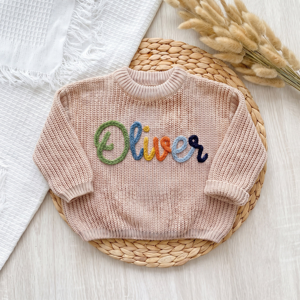 Beige personalized baby sweater with hand embroidered multicolor yarn name Oliver, laid flat