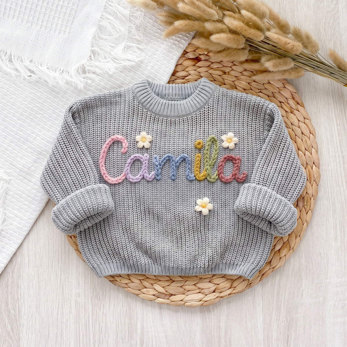 Sky grey personalized sweater with hand embroidered pastel yarn name Camila and flowers, laid flat