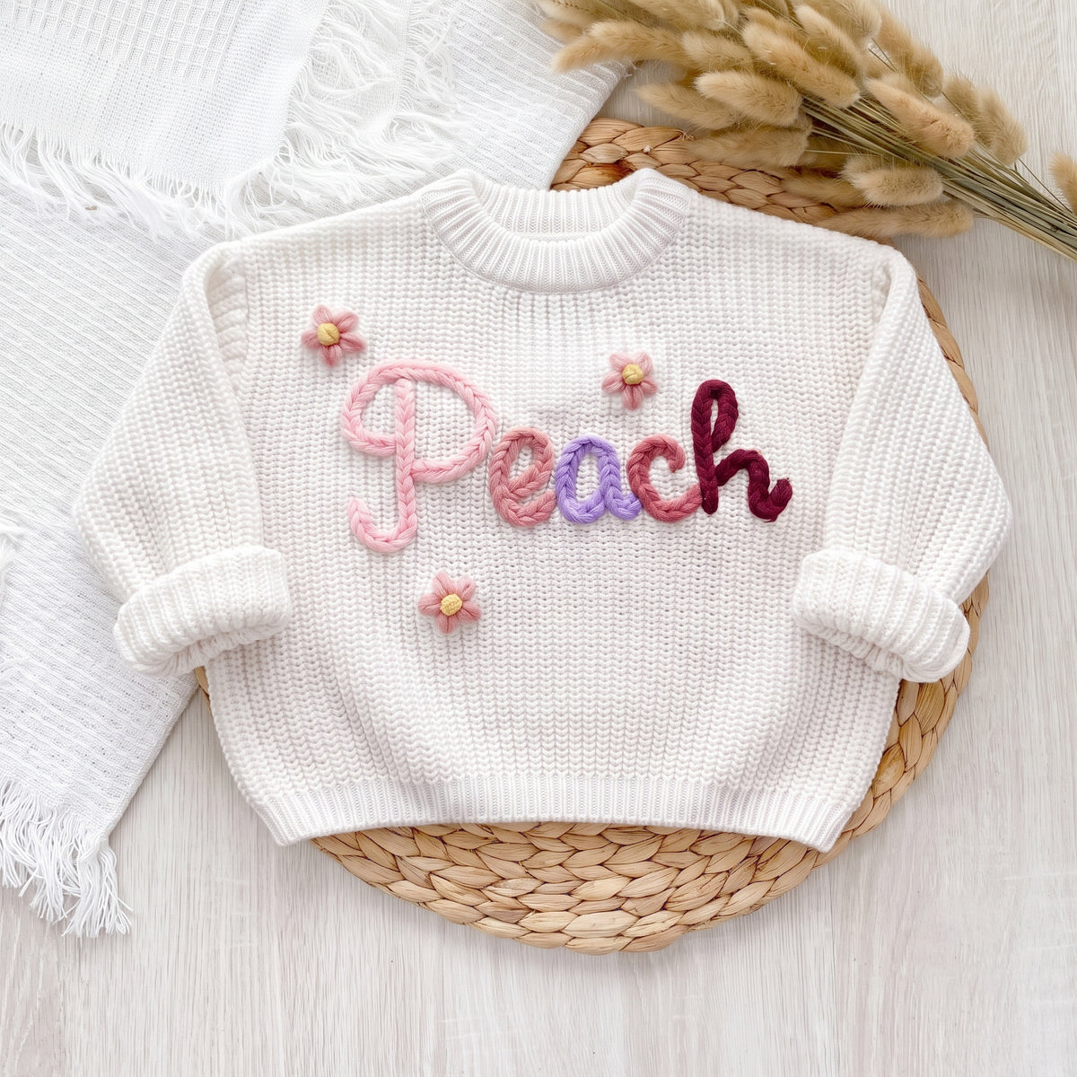 White personalized sweater with hand embroidered yarn name Peach and flowers, laid flat