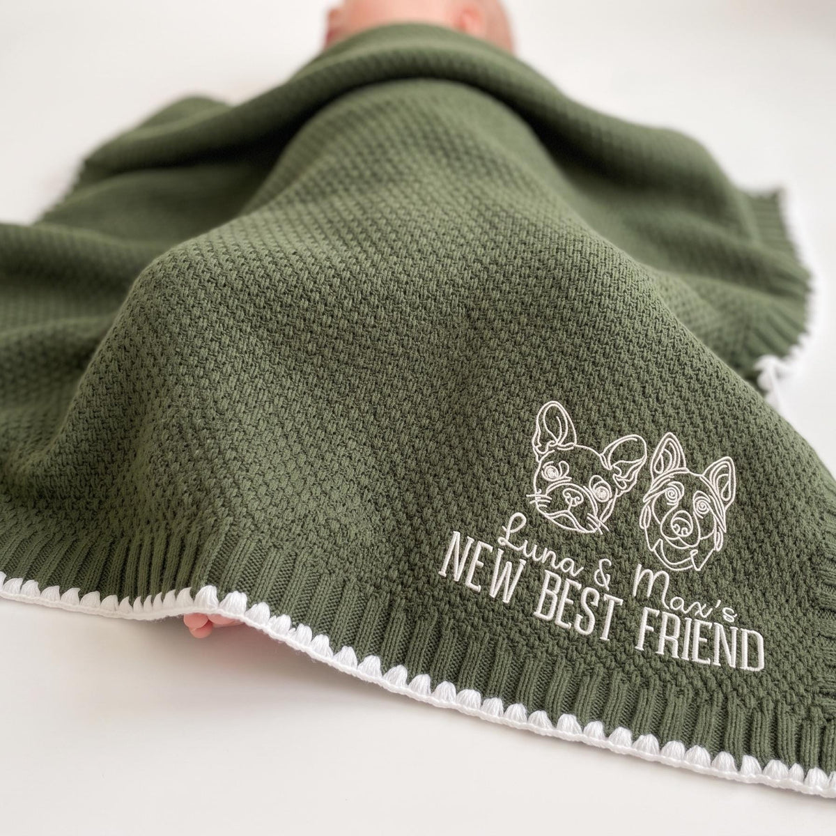 Baby under an olive custom pet baby blanket embroidered with dog and cat portraits and "New Best Friend"