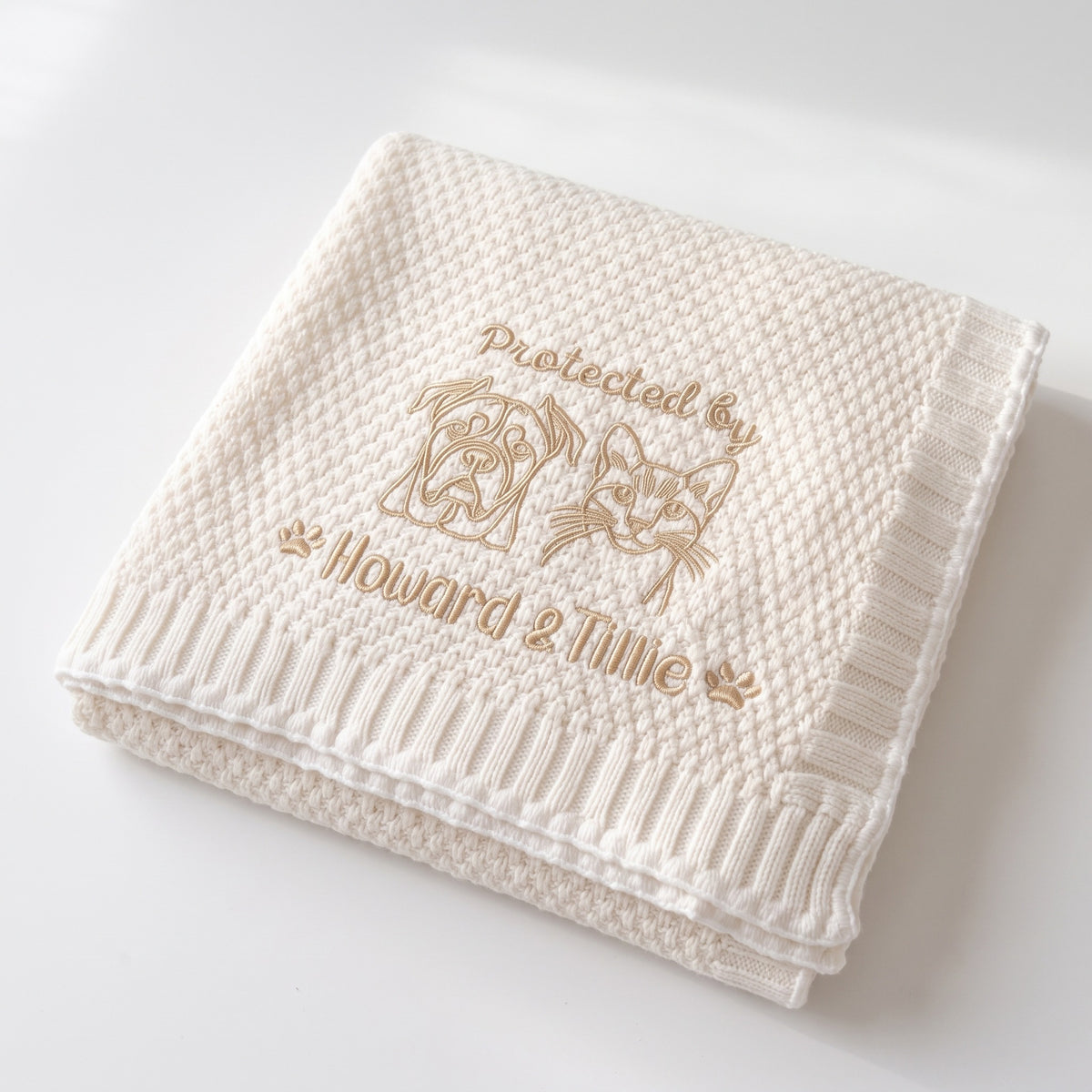 Folded white custom pet baby blanket with embroidered dog and cat portraits and pet names