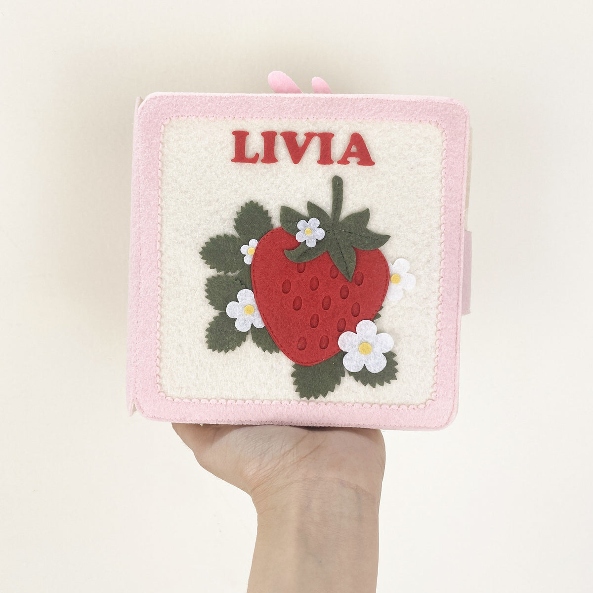 Hand holding a personalized strawberry felt quiet book with the name Livia